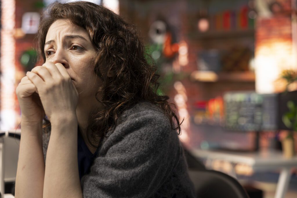 Woman sitting indoors with hands near her mouth during an emotional self-check for woman, appearing anxious and deep in thought.