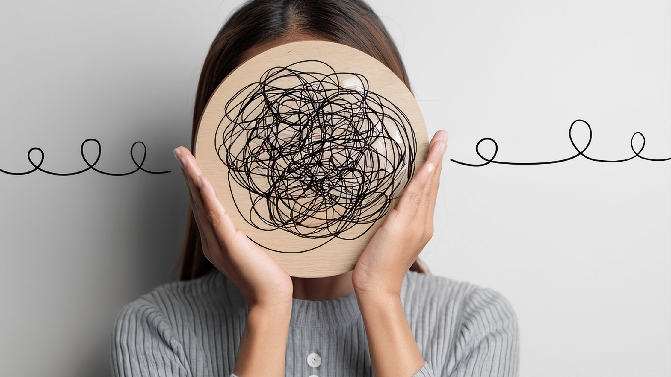 Woman holding a circular board with tangled black lines in front of her face, representing mental overwhelm and racing thoughts.
