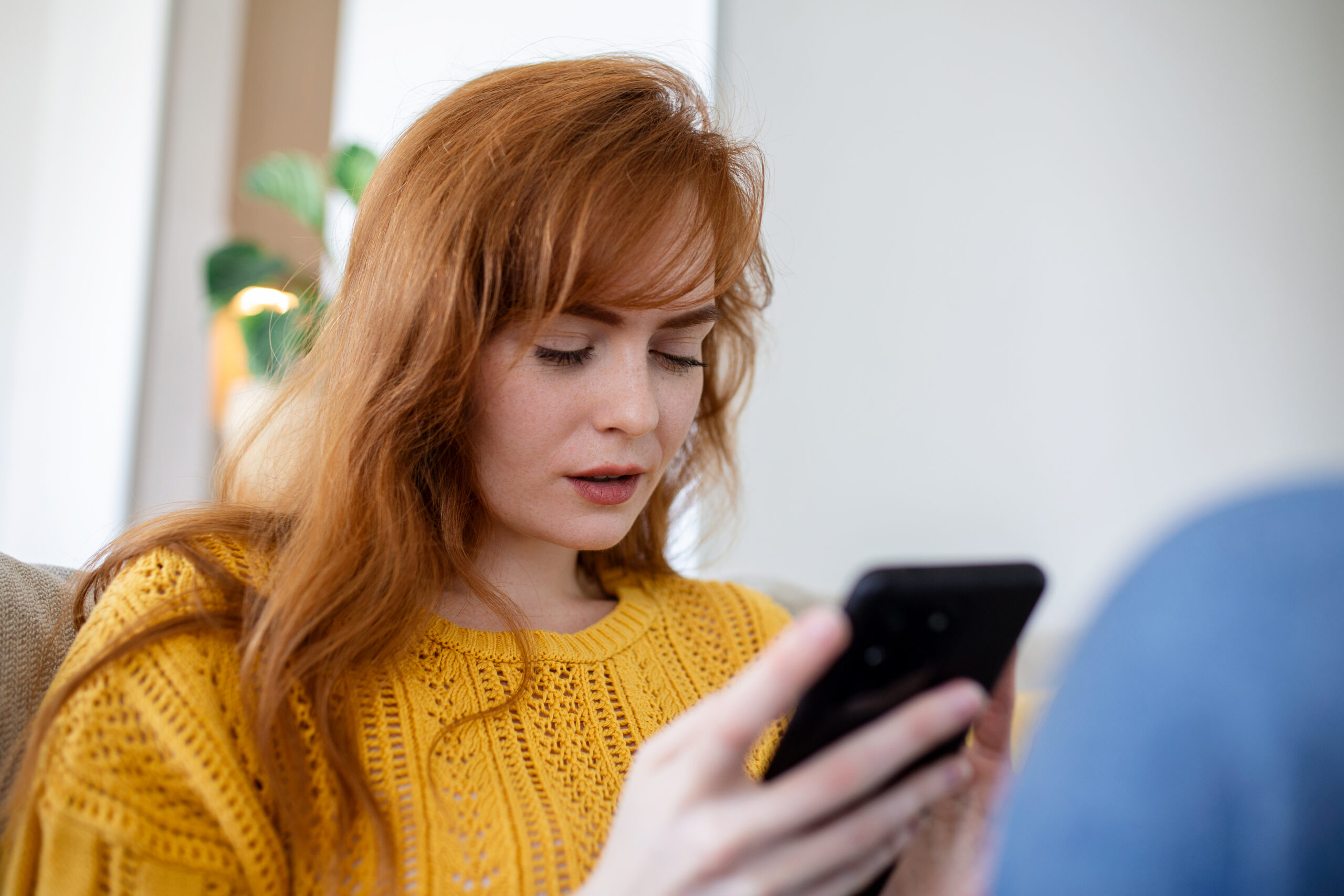 Woman sitting at home and looking at her smartphone while researching health information online.