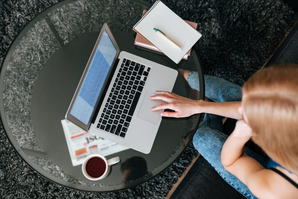 Woman using a laptop at a table with a notebook and cup of tea nearby.